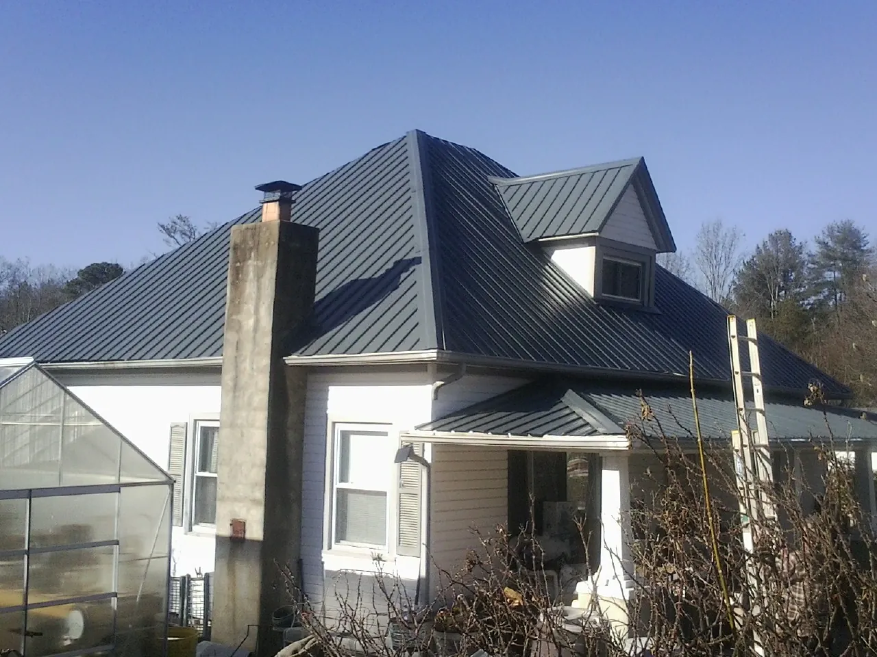 Dark blue standing seam metal roof on a white farmhouse with dormer — Slate & Tile Roof Repair by Roofing Brothers in Martin
