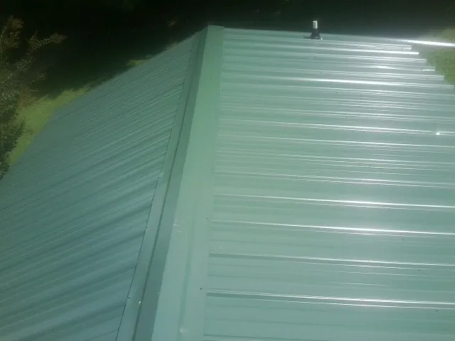 New green metal panels meeting at the ridge of a roof — Flat Roof Repair work by our crew in Martin