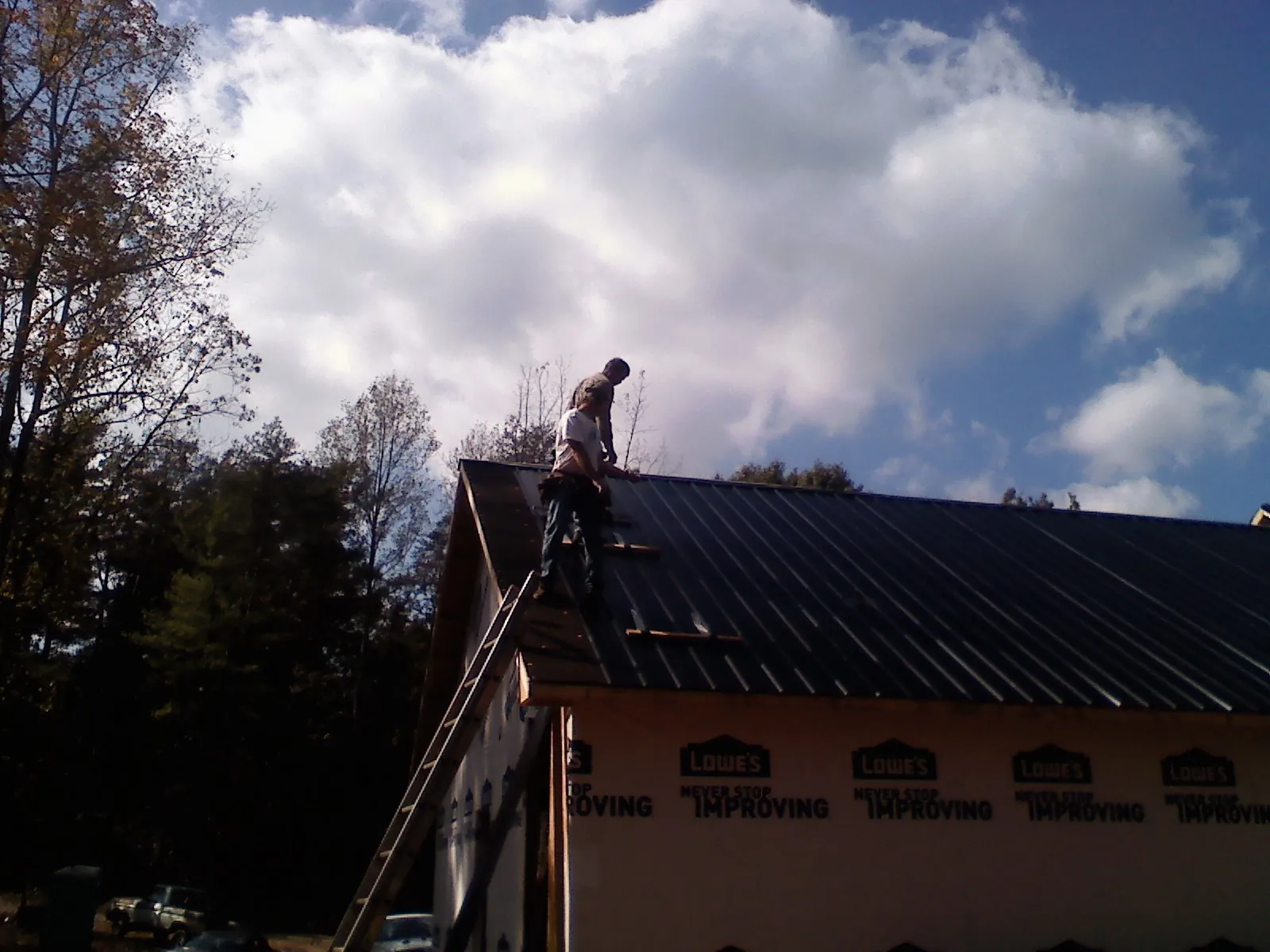 Roofer fastening dark metal panels high against a cloudy sky, from a Roof Inspection job in Martin