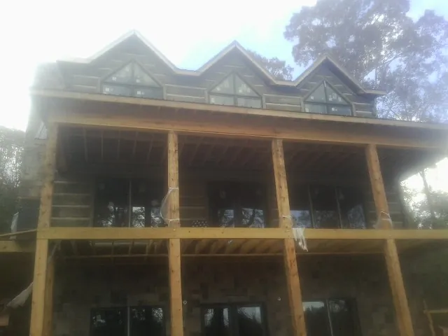 Dormers and porch framing on a large log home under construction — Roof Coating work by our crew in Martin